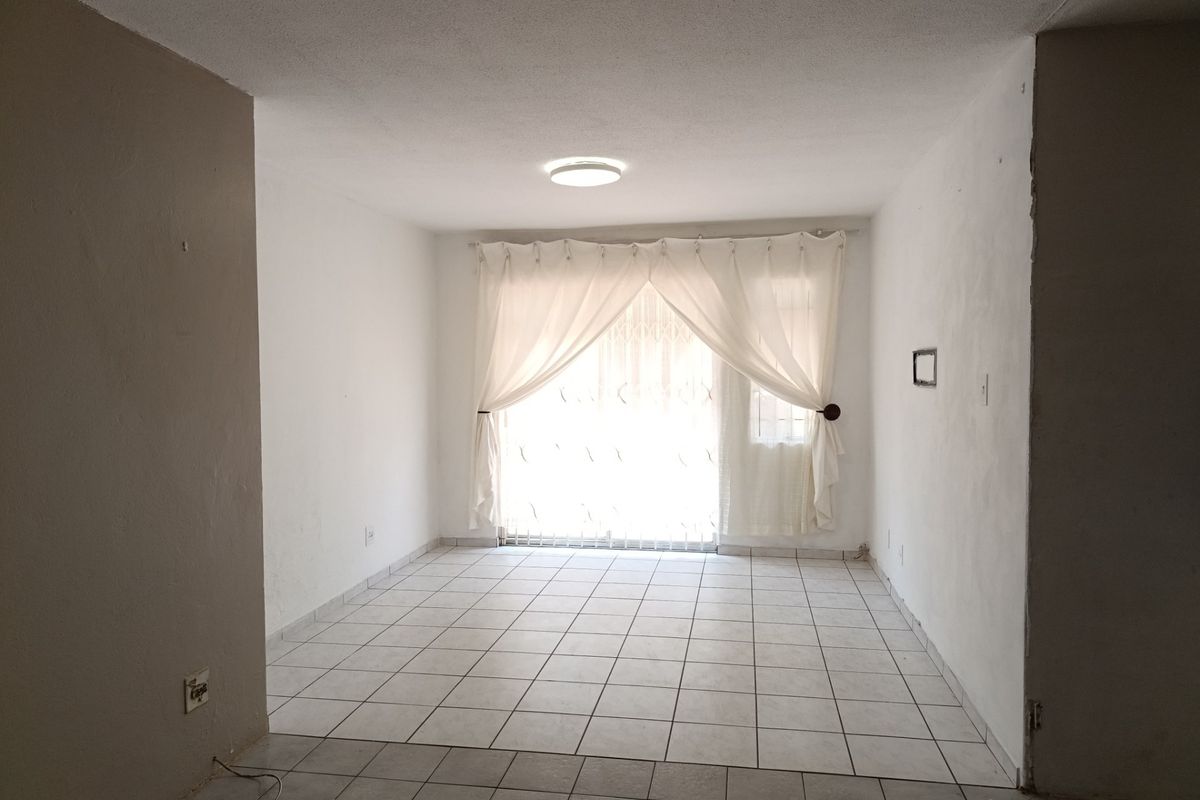 An empty living room featuring tiled flooring, a ceiling light fixture, and a sliding glass door with an integrated security gate.