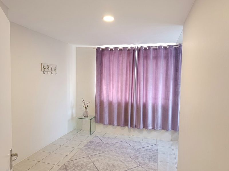 A bright, neutral bedroom featuring tiled flooring and recessed ceiling lighting, offering a clean and versatile space ready for personalization.