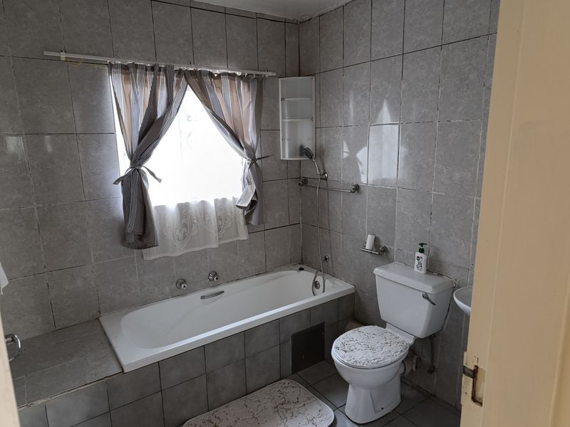 A functional bathroom featuring full-height wall tiling, a standard bathtub with shower mixer, and a toilet.