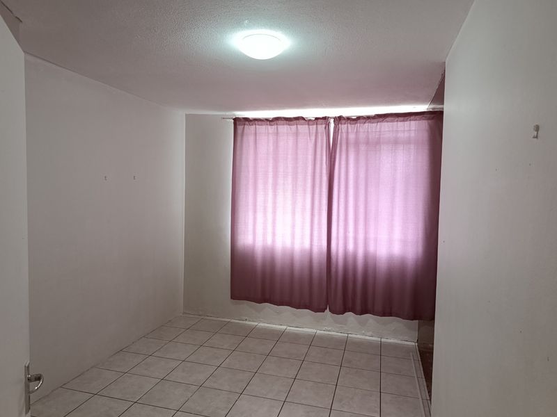An empty bedroom featuring tiled flooring and a ceiling light fixture, ready for renovation or staging.