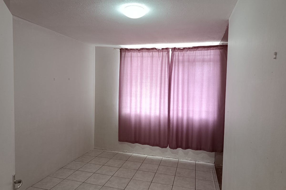An empty bedroom featuring tiled flooring and a ceiling light fixture, ready for renovation or staging.