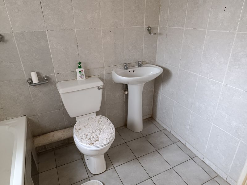 A functional bathroom featuring a pedestal washbasin, toilet, and bathtub with full-height ceramic wall tiling and tiled flooring.