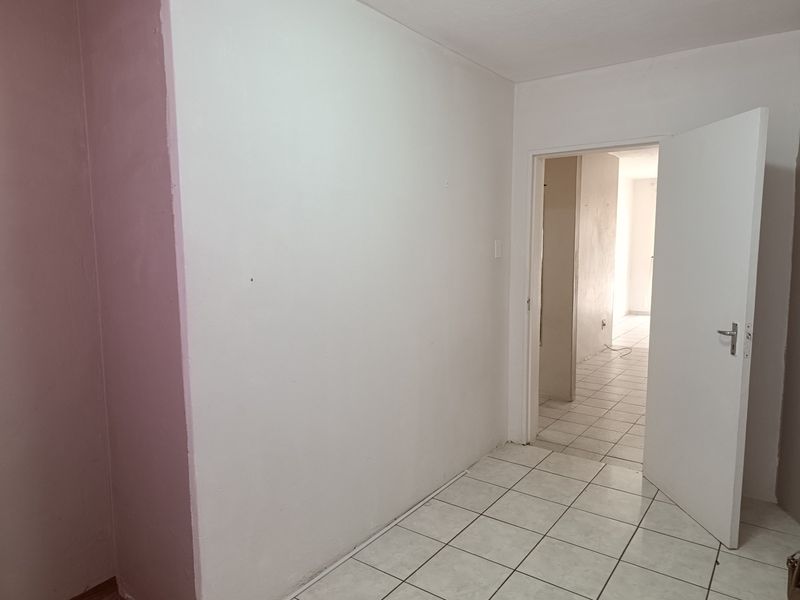 An empty bedroom featuring tiled flooring and a white internal door, showing signs of wear on the walls.