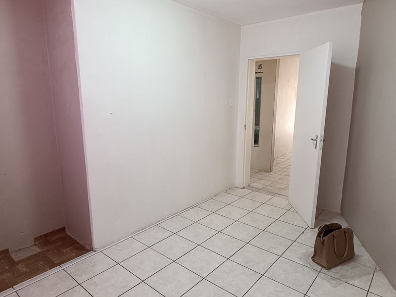 An empty bedroom featuring white walls and ceramic floor tiles, providing a blank canvas for potential interior design and renovation.