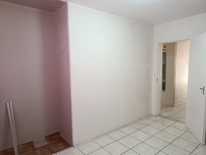 An empty bedroom featuring tiled flooring and a built-in alcove, offering a blank canvas for renovation or interior design updates.