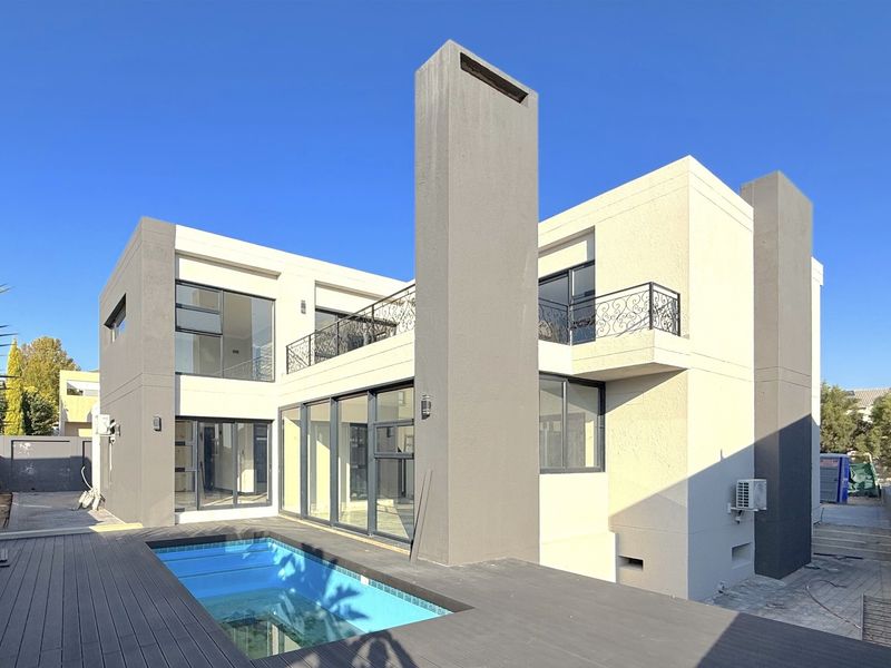 Modern double-story rear elevation featuring a swimming pool, timber decking, large sliding glass doors, and a balcony with decorative wrought iron railings.