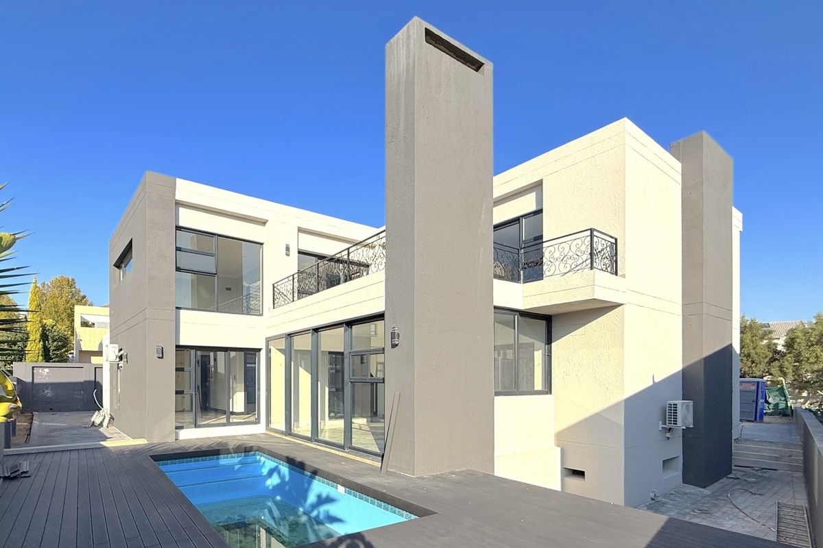 Modern double-story rear elevation featuring a swimming pool, timber decking, large sliding glass doors, and a balcony with decorative wrought iron railings.