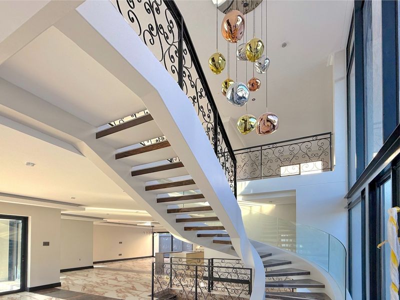 Grand entrance hall featuring a striking floating staircase with wrought iron balustrades, marble flooring, and a double-volume ceiling with modern pendant lighting.