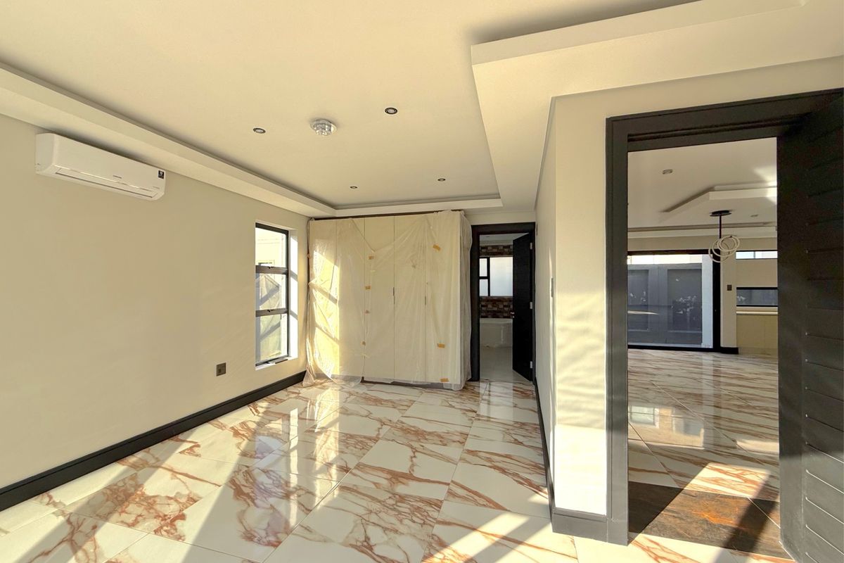 A bright, modern bedroom featuring polished marble-look porcelain floor tiles, recessed ceiling lighting, and a wall-mounted air conditioning unit.