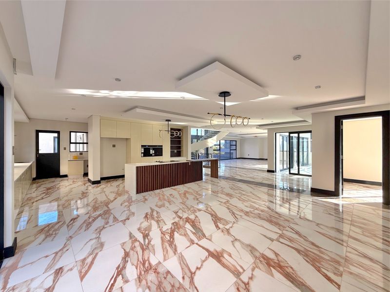 Spacious open-plan living and kitchen area featuring high-end marble-look floor tiles, modern kitchen island, and abundant natural light through large sliding glass doors.