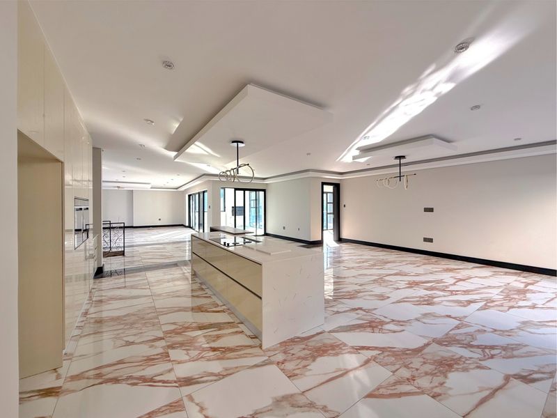Spacious open-plan living and kitchen area featuring high-gloss cabinetry, a central island, and elegant marble-look flooring with modern recessed ceiling details.