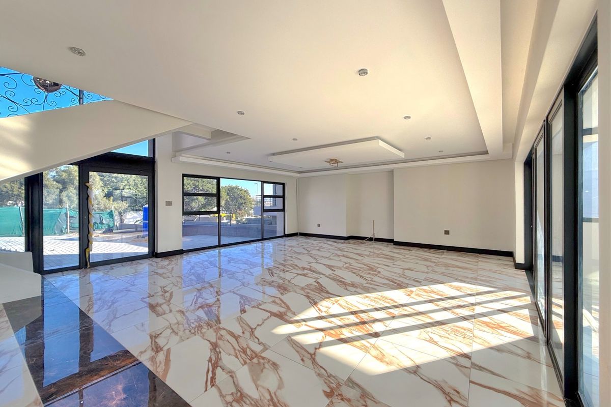 Spacious, modern open-plan living area featuring high-gloss marble-look floor tiles, recessed ceiling lighting, and expansive glass sliding doors leading to the exterior.