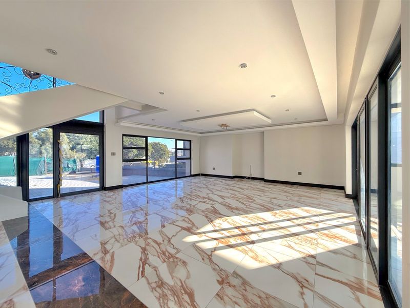 Spacious, modern open-plan living area featuring high-gloss marble-look floor tiles, recessed ceiling lighting, and expansive glass sliding doors leading to the exterior.