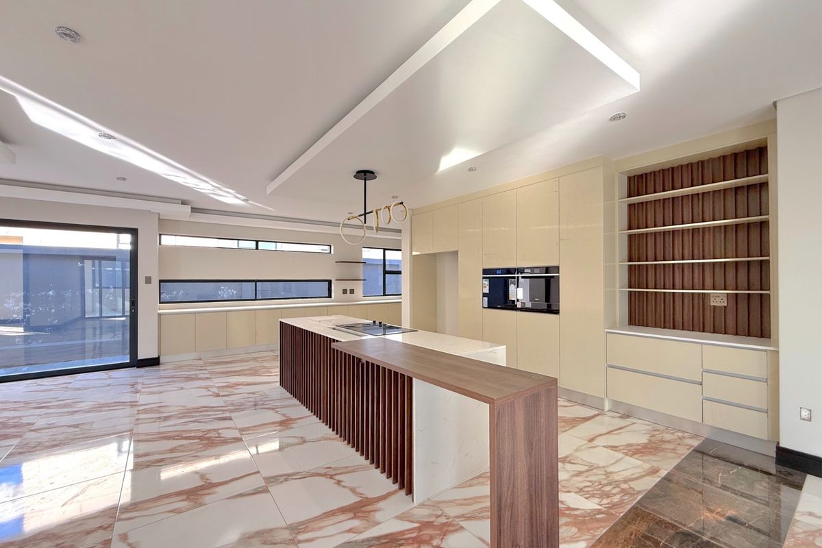 Modern, spacious kitchen featuring a large island with breakfast bar, integrated appliances, high-gloss cabinetry, and elegant marble-look flooring.