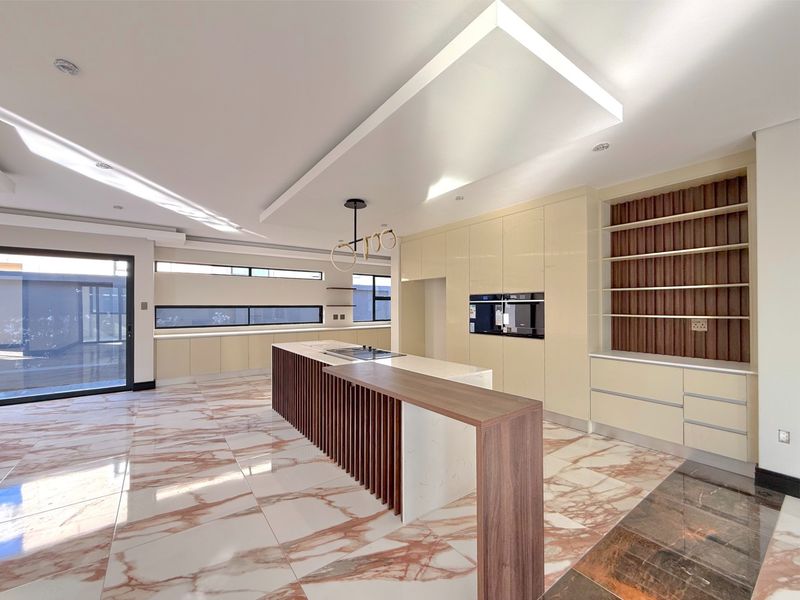 Modern, spacious kitchen featuring a large island with breakfast bar, integrated appliances, high-gloss cabinetry, and elegant marble-look flooring.
