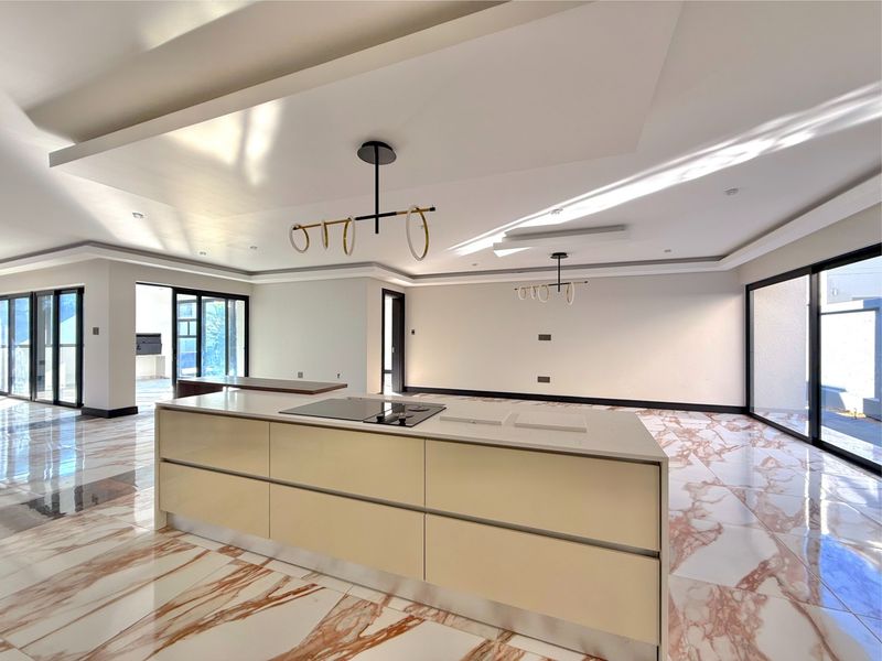 Spacious open-plan living area featuring a modern kitchen island with built-in hob, stone countertops, and elegant marble-look flooring with large sliding glass doors.