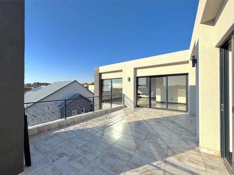 A spacious, modern balcony featuring tiled flooring, decorative wrought iron railings, and large sliding glass doors providing seamless indoor-outdoor flow.