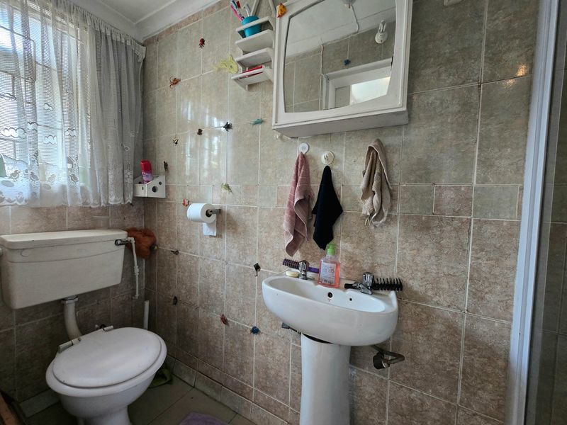 A functional bathroom featuring a pedestal basin, toilet, and tiled walls. The space would benefit from modern updates to finishes and fixtures.