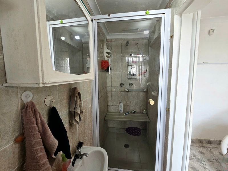 Compact bathroom featuring a tiled shower enclosure with a built-in bench, wall-mounted vanity cabinet, and neutral ceramic wall and floor tiling.