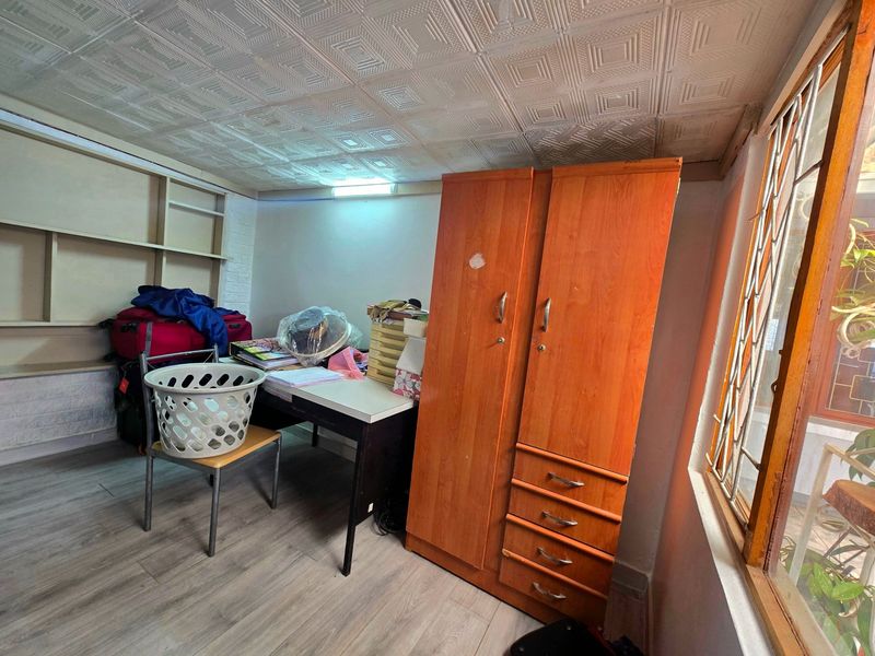 A bedroom featuring textured ceiling tiles, built-in shelving, and a window with a security gate, requiring cosmetic updates to improve its overall condition.
