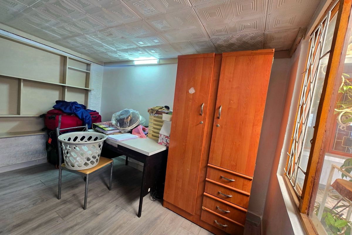 A bedroom featuring textured ceiling tiles, built-in shelving, and a window with a security gate, requiring cosmetic updates to improve its overall condition.