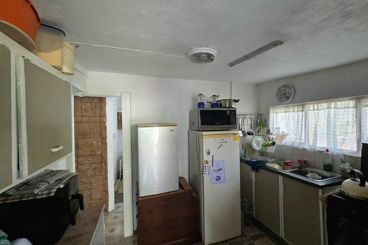 A functional kitchen space featuring original cabinetry, a stainless steel sink, and tiled flooring, currently showing signs of age and wear.
