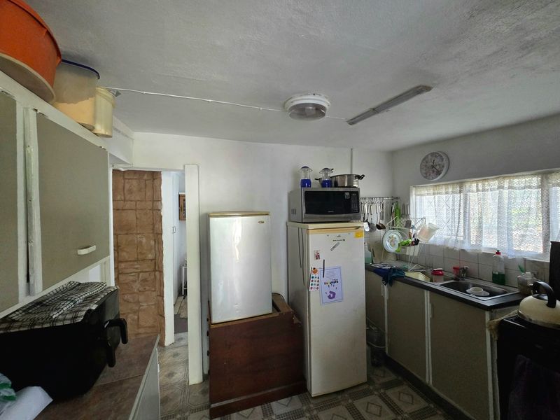 A functional kitchen space featuring original cabinetry, a stainless steel sink, and tiled flooring, currently showing signs of age and wear.