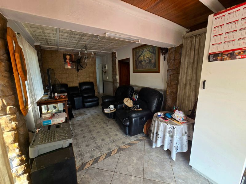 A living area featuring stone-clad pillars, timber ceiling accents, and decorative ceiling tiles, offering a dated aesthetic with potential for modernization.