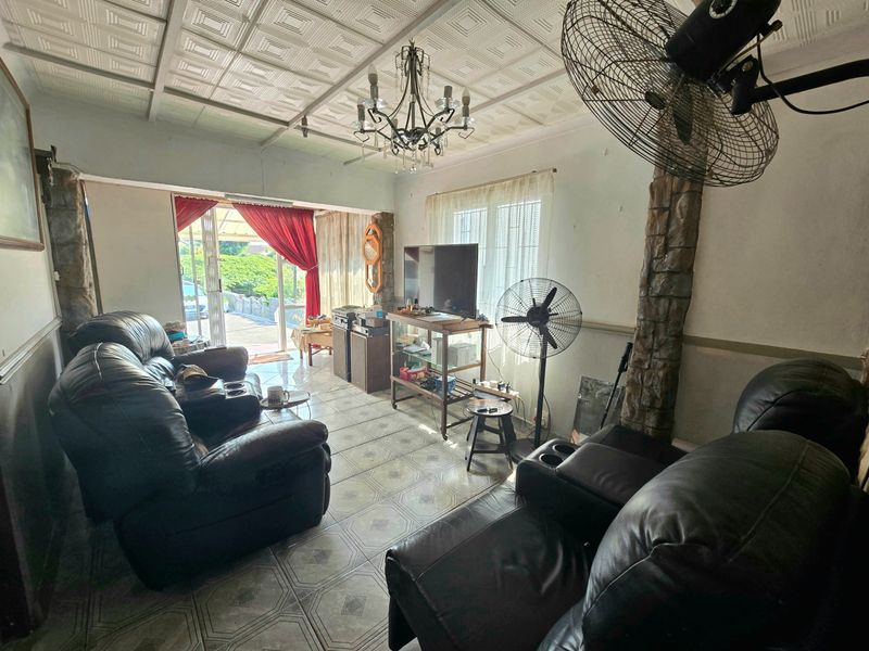 A living room featuring tiled flooring, decorative ceiling tiles, and stone-clad pillars, with direct access to an outdoor area through a sliding glass door.