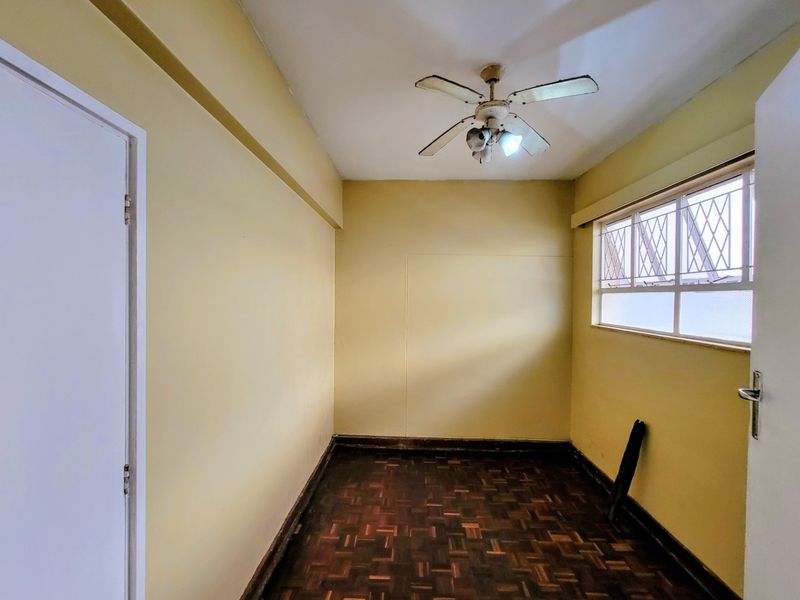 An empty bedroom featuring parquet flooring, a ceiling fan, and a window with security bars.