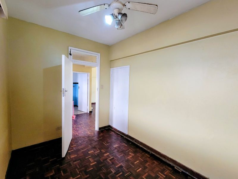 An empty bedroom featuring traditional parquet flooring, a ceiling fan, and a built-in cupboard, offering a blank canvas for renovation.