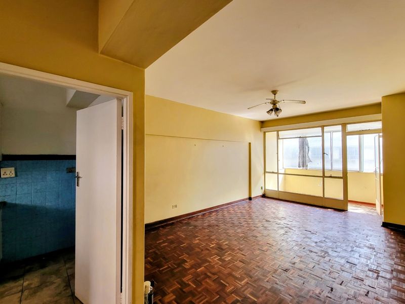 Spacious living area featuring original parquet flooring, a ceiling fan, and direct access to an enclosed balcony, offering a blank canvas for renovation.