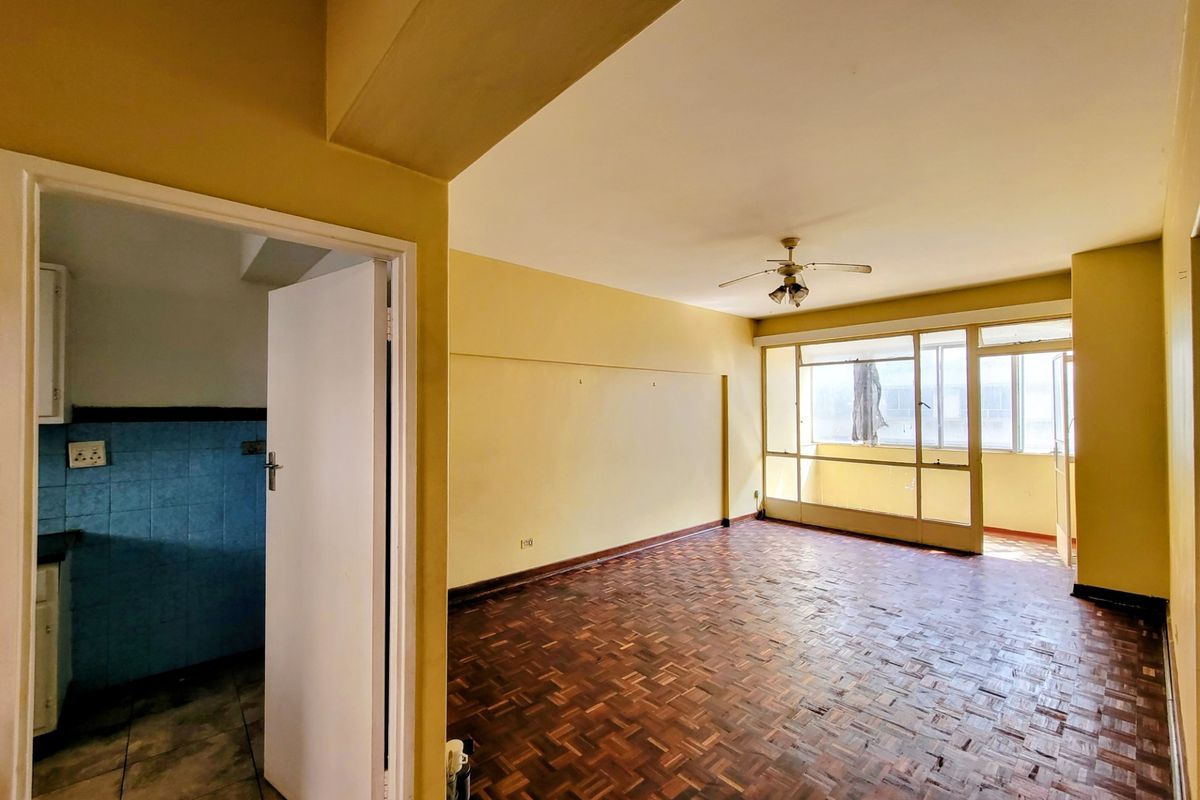 Spacious living area featuring original parquet flooring, a ceiling fan, and direct access to an enclosed balcony, offering a blank canvas for renovation.