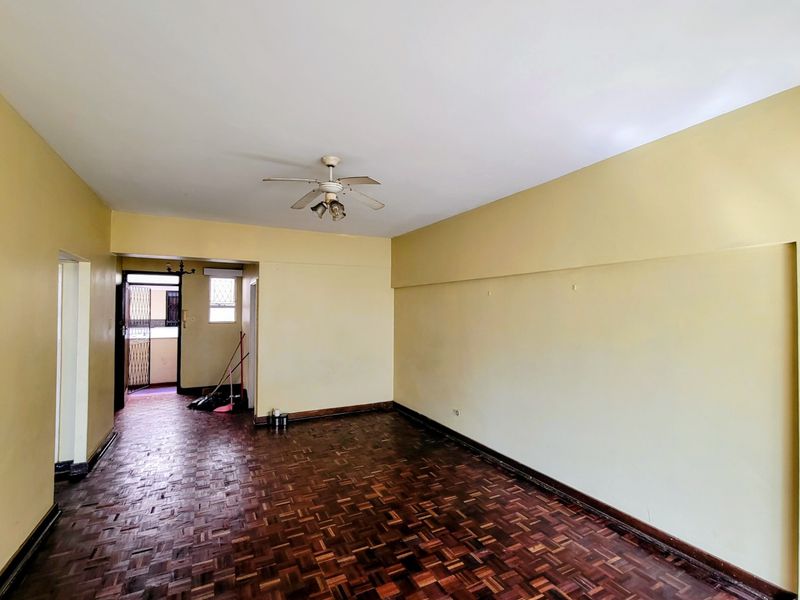 Spacious living area featuring original parquet flooring, a ceiling fan, and neutral wall tones, leading to an external security gate entrance.