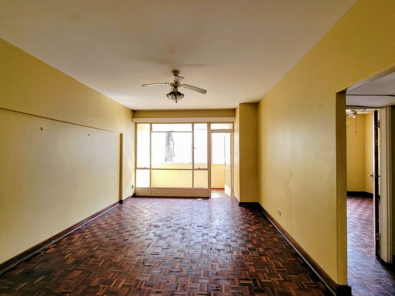An empty living room featuring original parquet flooring, a ceiling fan, and direct access to an attached balcony through a sliding glass door.