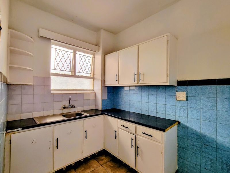 A compact, dated kitchen featuring white built-in cabinetry, dark countertops, and blue tiled splashbacks, offering a functional layout ready for modernization.