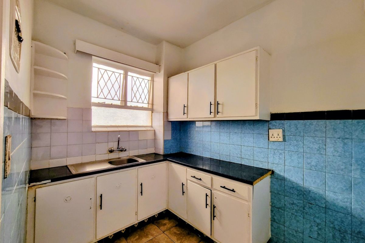 A compact, dated kitchen featuring white built-in cabinetry, dark countertops, and blue tiled splashbacks, offering a functional layout ready for modernization.