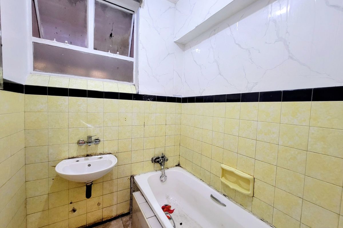 A dated bathroom featuring a wall-mounted basin, bathtub, and tiled walls. The space requires renovation to update the finishes and address visible wear.