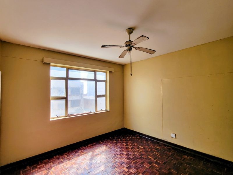 An empty bedroom featuring original parquet flooring, a ceiling fan, and a large metal-framed window with natural light.