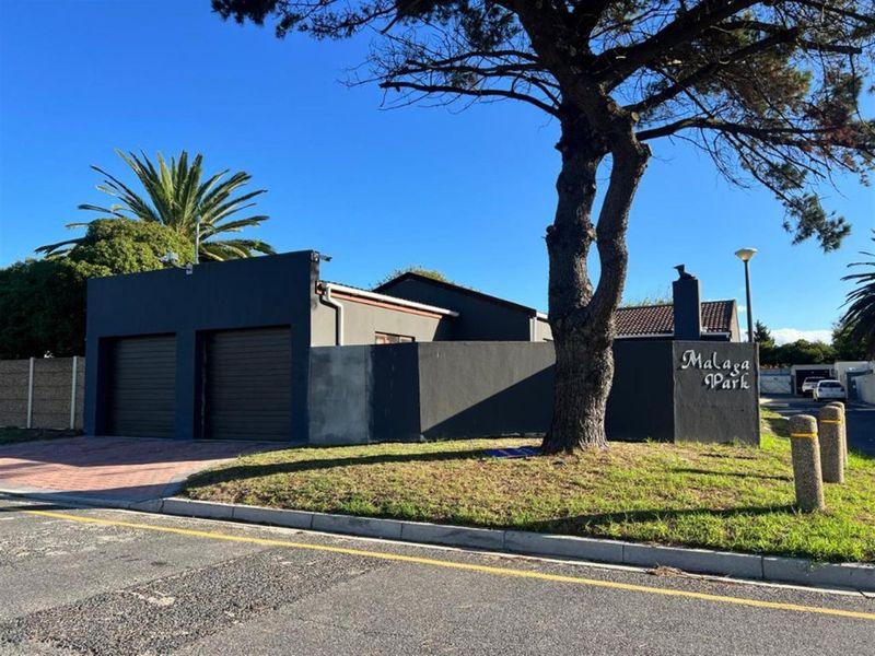 Front exterior view of the property featuring a double garage, paved driveway, and a boundary wall with signage.