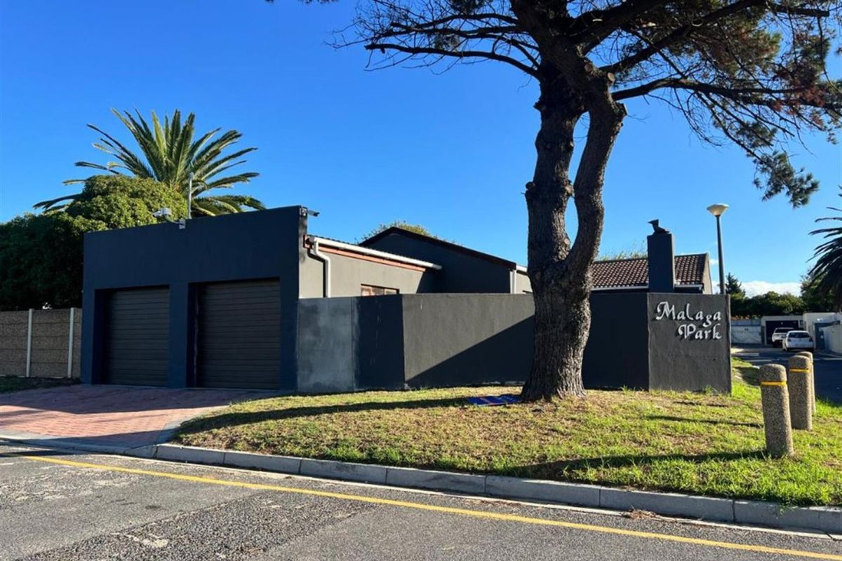 Front exterior view of the property featuring a double garage, paved driveway, and a boundary wall with signage.