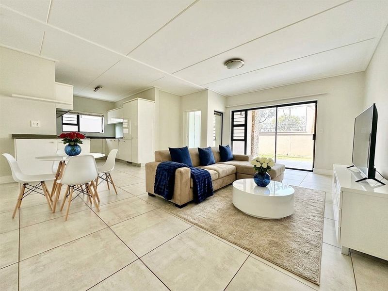 Bright open-plan living and kitchen area featuring neutral tiled flooring, modern cabinetry, and large sliding glass doors leading to an outdoor space.