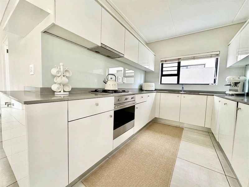 Modern kitchen featuring sleek white cabinetry, stone countertops, glass splashback, and integrated stainless steel appliances including a gas hob and oven.