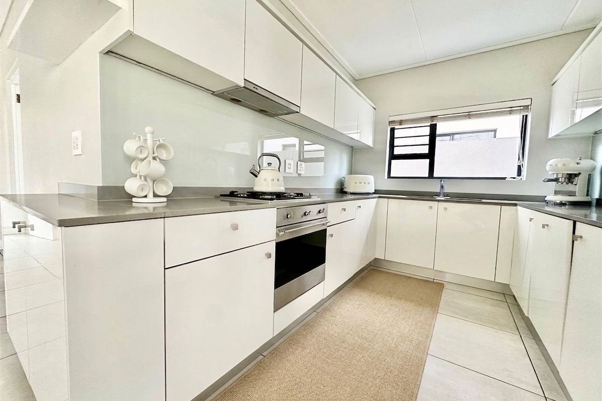 Modern kitchen featuring sleek white cabinetry, stone countertops, glass splashback, and integrated stainless steel appliances including a gas hob and oven.