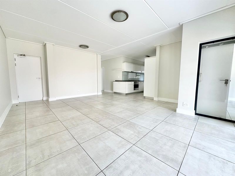 Spacious open-plan living area featuring neutral tiled flooring and a modern kitchen with built-in cabinetry, oven, and hob.