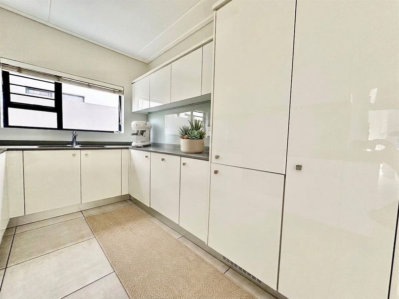 Modern kitchen featuring sleek white glossy cabinetry, stone countertops, integrated storage, and tiled flooring with a functional layout.
