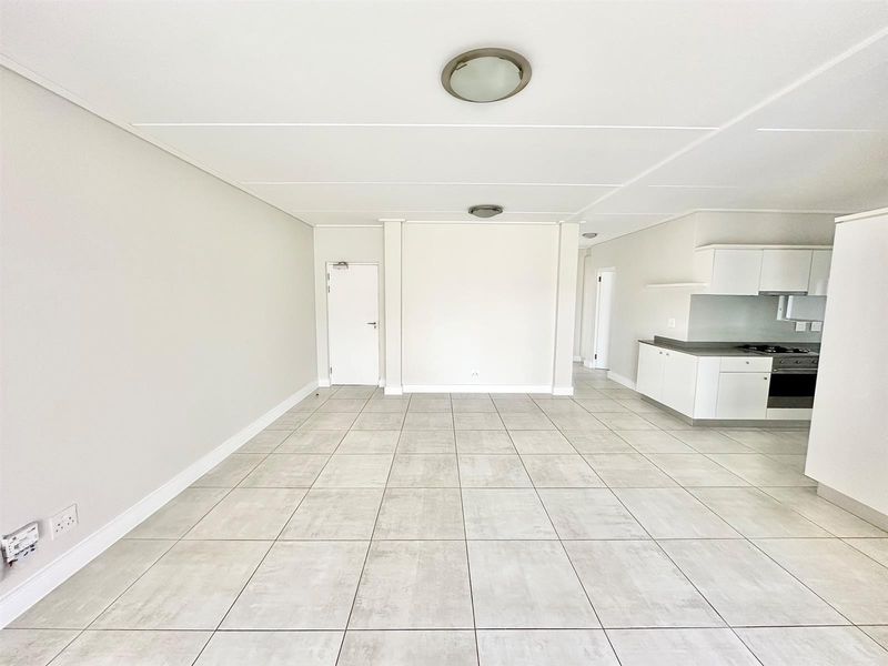 Spacious open-plan living area featuring neutral tiled flooring and a modern kitchen with built-in cabinetry, oven, and hob.