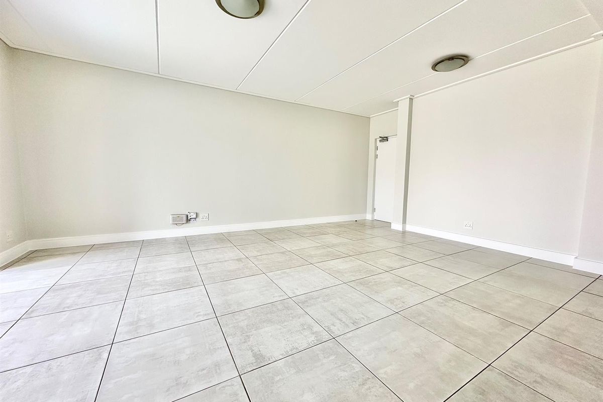 A bright, spacious, and empty living area featuring neutral tiled flooring, clean white walls, and modern flush mount ceiling lighting.