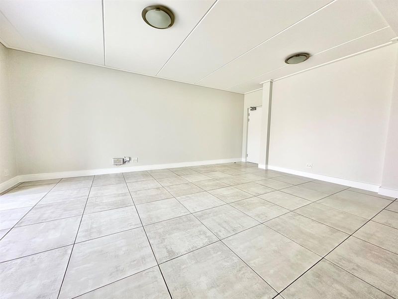 A bright, spacious, and empty living area featuring neutral tiled flooring, clean white walls, and modern flush mount ceiling lighting.