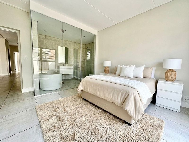 Modern bedroom featuring a sleek glass-enclosed en-suite bathroom with a freestanding bathtub and walk-in shower, complemented by neutral tiled flooring.